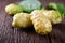 Whole fresh noni fruit with leaf on wooden table