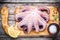 Whole fresh raw octopus with sea salt and lemon on cutting board