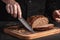 Whole grain bread put on kitchen wood plate with a chef holding gold knife for cut. Fresh bread on table close-up