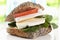Whole grain bread with soft cheese, tomato and lamb`s lettuce on chopping board, close up.