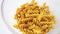 Whole grain dark yellow uncooked fusilli pasta. Italian macaroni falling in a pile in a transparent plate close up