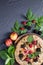 Whole-grain galette with plums and berries on dark background, t