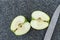 Whole Granny Smith apple sliced in half on a plastic man made faux gray granite cutting board, chefs knife