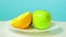 A whole green apple and a half of kiwi and orange on a white plate rotate in a circle