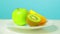 A whole green apple and a half of kiwi and orange on a white plate rotate in a circle