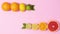 Whole and half citrus fruits ordering in line with green leaves on pastel pink background. Stop motion