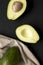Whole and halved avocados over black surface, top view. From above, overhead, flat lay