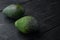 Whole pair of green avocado, on black wooden background