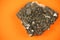 Whole piece of black lead ore block formation with irregular texture, shot on orange paper background