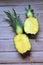 Whole pineapple cut in half, two pieces of pineapple halves, pineapple fruit on wooden background, yellow fruit