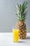 Whole Pineapple Tall Glass with Freshly Pressed Orange Citrus Juice on White Kitchen Table Grey Stone Wall. Vitamins Morning