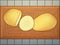 Whole potato, potato cut in half and slice of potato on a wooden cutting board