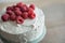 Whole raspberry cake with white frosting and fresh raspberries.