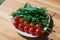 Whole red tomato cherry and fresh ruby leaves composition on a white plate on the wooden table