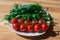 Whole red tomato cherry and fresh ruby leaves composition on a white plate on the wooden table