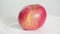 Whole ripe pink apple fruit on white plate rotates