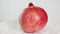 Whole ripe pink pomegranate fruit on white plate rotates