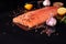 Whole salmon fillet on a dark background, sprinkled with multicolored peppercorns with garlic, rosemary and lemon