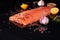 Whole salmon fillet on a dark background, sprinkled with multicolored peppercorns with garlic, rosemary and lemon