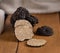 Whole and sliced black truffles mushroom on wooden board on dark brown table, close up