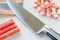 Whole and sliced surimi crab sticks and sharp chef knife on a white kitchen table. Seafood and ingredient for salads. Healthy