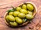 Whole table olives in the wooden bowl on the table.