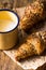 Whole wheat croissants on parchment paper, enamel mug with milk on wood kitchen table in morning light