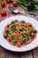 Whole wheat spaghetti with ramsons, tomatoes and olives on wood table
