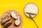 Wholegrain bread on cutting board with butter on plate, slice of bread with butter on yellow background top view