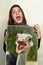 Whose mouth is bigger. Portrait of a young woman holding a photo of an ostrich with its mouth wide open.