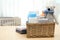Wicker basket with baby cosmetic products, toy and towels on table indoors.