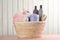 Wicker basket full of different baby cosmetic products, accessories and toy on pink wooden table