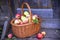 A wicker basket with rosy apples on a wooden porch surrounded by flowers.