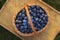 Wicker basket of tasty ripe blueberries on wooden surface outdoors, top view. Seasonal berries