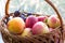 Wicker basket with washed fruits from new harvest in it. Ripe red apples, peach, and plums, water droplets on them.