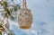 A wicker beige lantern with a white candle inside hanging on a rough brown rope