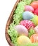 Wicker bowl with colorful Easter eggs on white background, closeup