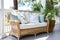 Wicker couch with textile cushions. Green potted plants flowers. Colonial style residential house. Sunny day. Cozy atmosphere.