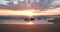 Wide angle beach at sunset with sun reflected on ocean and waves splashing over rocks.