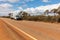 Wide angle Landscape view of 4WD and modern caravan on an outback highway in Australia under a blue cloudy sky