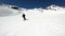 A wide angle male skier aged in black equipment and white helmet with ski poles rides on a snowy slope on a sunny day