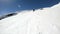 A wide angle male skier aged in black equipment and white helmet with ski poles rides on a snowy slope on a sunny day