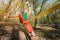 Wide angle male tightrope walker balancing while sitting barefoot on slackline in autumn forest. The concept of outdoor