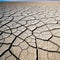 An wide angle shot of an expanse of cracked parched earth from a low blue sky and horizon in the distance