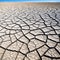 An wide angle shot of an expanse of cracked parched earth from a low blue sky and horizon in the distance