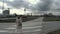 Wide angle shot of A girl from rear in winter clothes walking on zebra road cross against dramatic stormy and windy weather,