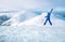 Wide angle shot of woman dressed in ski warm clothing jumping on the mountain peak with snowy range and valley on the background.