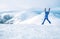 Wide angle shot of woman dressed in ski warm clothing jumping on the mountain peak with snowy range and valley on the background.