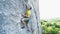 Wide angle view of man rock climber in yellow t-shirt, climbing on a cliff, on tough sport route, resting and chalking