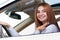 Wide angle view of young redhead woman driver fastened by seatbelt driving a car smiling happily